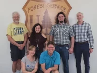 Na zdjęciu widoczna grupa osób na tle logo United States Forest Service.